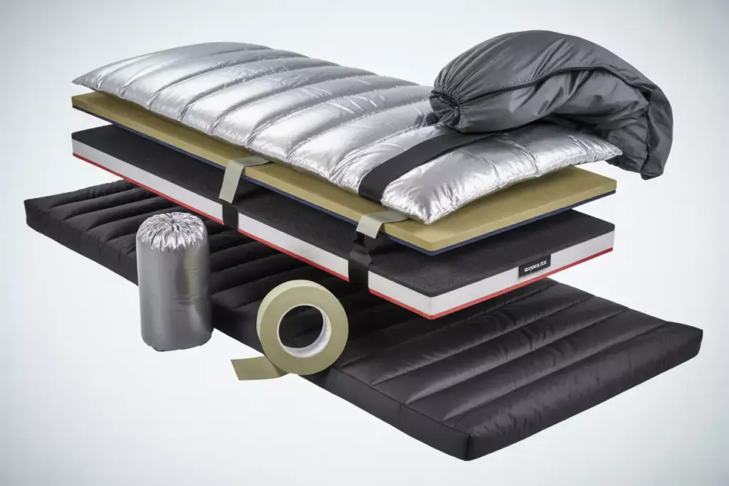 A futuristic, layered sleeping bag and mat set with metallic and black elements, shown in an exploded view.