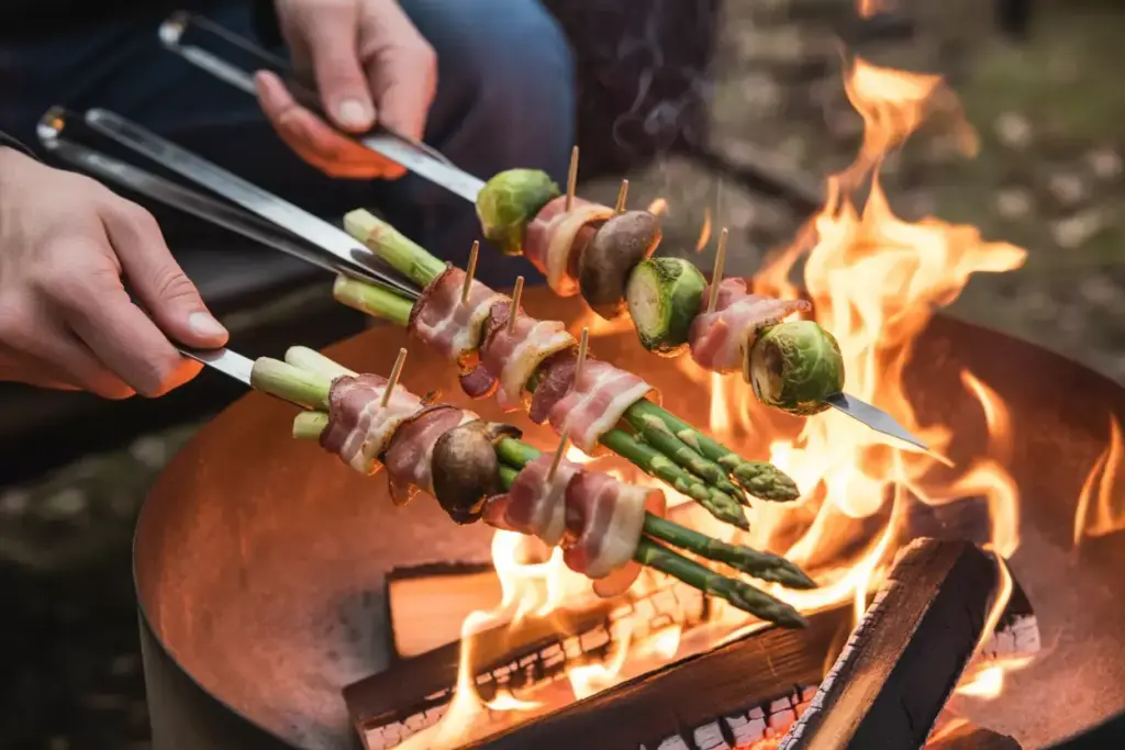 3 Bacon Wrapped Vegetable Skewers Sizzling Over Fire Pit Flames With Asparagus And Mushrooms