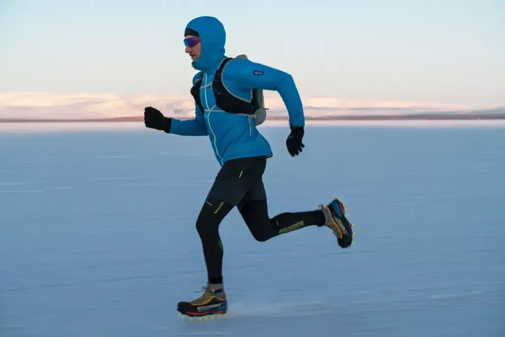 Person in winter gear running across a snowy landscape with mountains in the background.