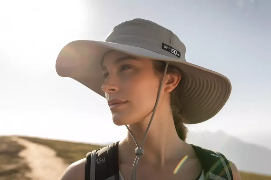 Woman wearing a wide-brimmed UPF 50+ hat outdoors, looking into the distance on a sunny day.