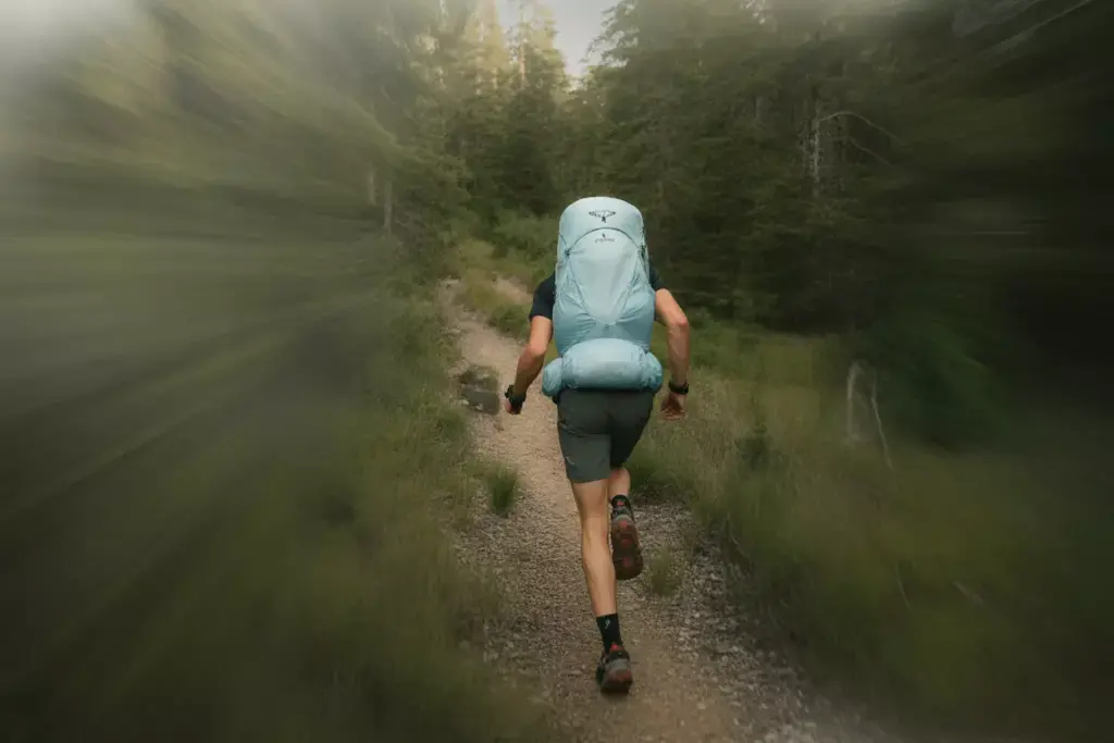 Person hiking quickly on a forest trail with a large blue backpack, motion blur around the edges.