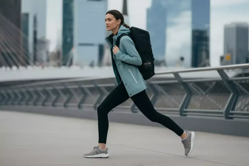 Woman in athletic wear lunging on a city bridge, with skyscrapers in the background and a backpack on her back.