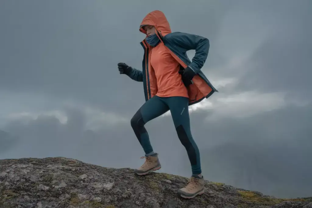 Person in outdoor gear hikes up a rocky slope on a cloudy, foggy day.