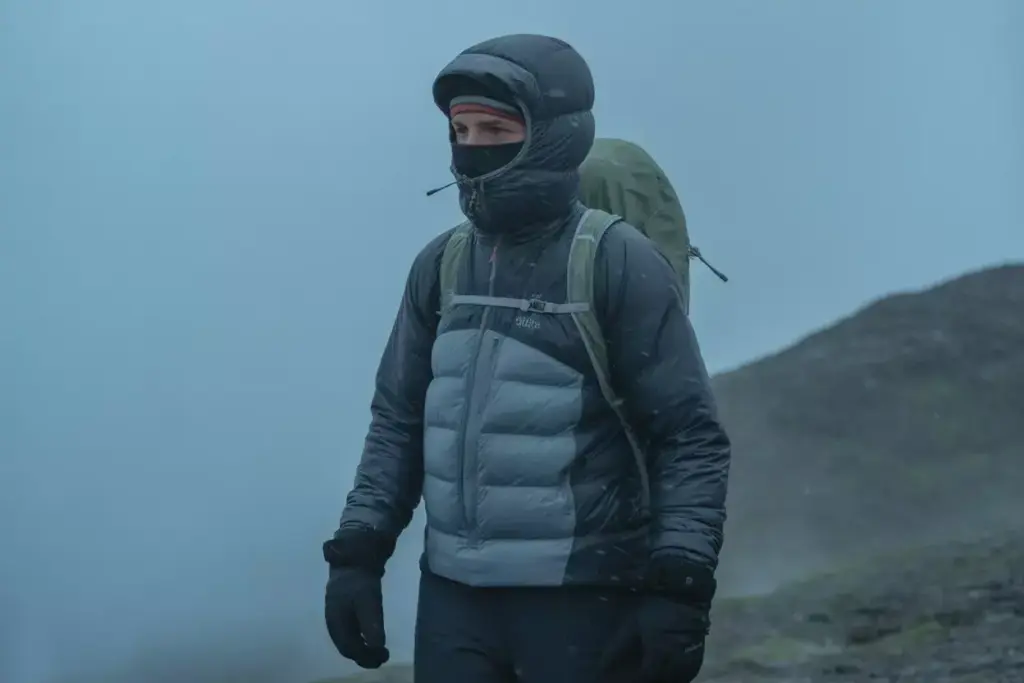 A hiker dressed in winter gear and a backpack walks through a foggy, mountainous landscape.