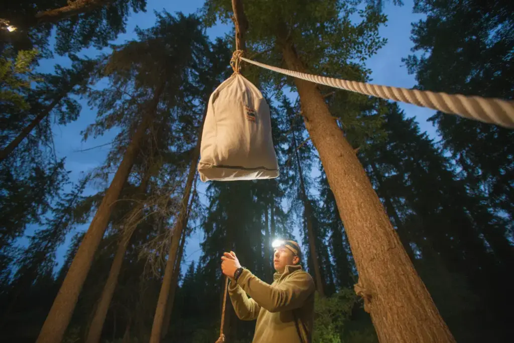 Bear Rope Hang Method Food Bag Suspended High In Forest At Dusk With Camper Securing Rope