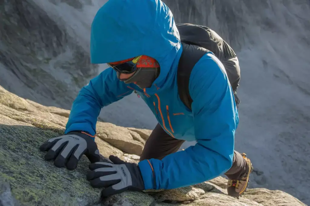 Technical Mountaineer In Hard Shell Gear Ascending Steep Rocky Terrain